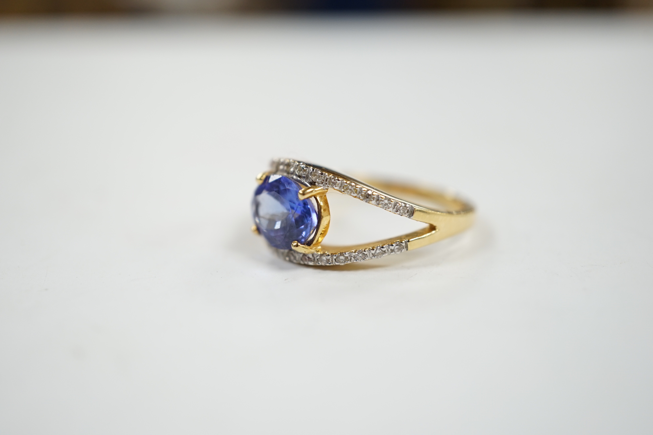 A modern 18ct gold and singe stone oval cut tanzanite ring, with diamond chip set borders, size N, gross weight 5 grams.